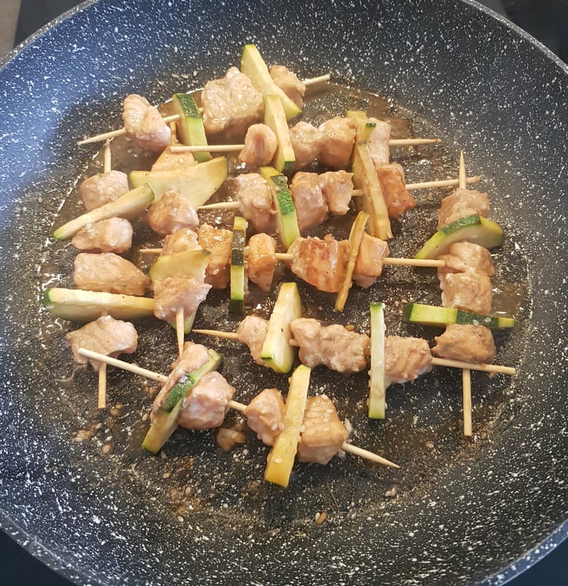 Cuisson des brochettes avec la marinade et du miel dans une grande poêle 